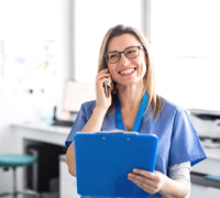 dental team member smiling while talking on phone and holding blue clipboard
